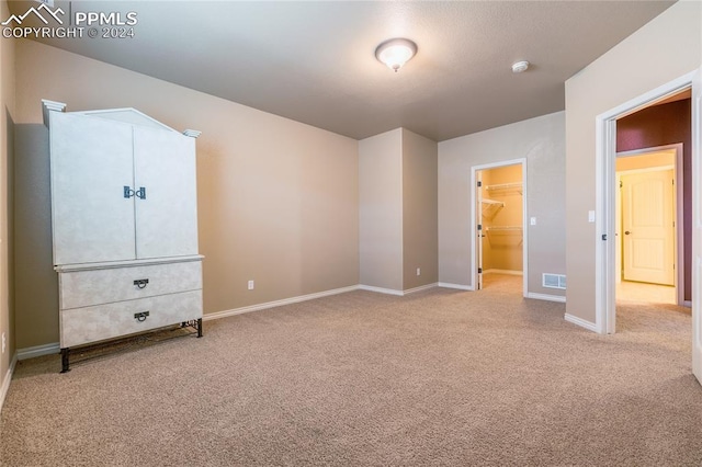 unfurnished bedroom featuring a walk in closet, light carpet, and a closet