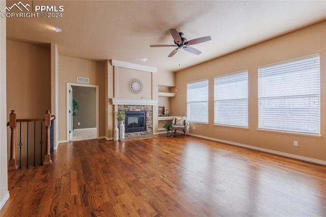 unfurnished living room with hardwood / wood-style flooring, ceiling fan, and a stone fireplace