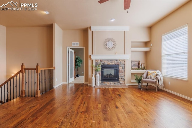 unfurnished living room featuring built in shelves, a stone fireplace, plenty of natural light, and wood-type flooring