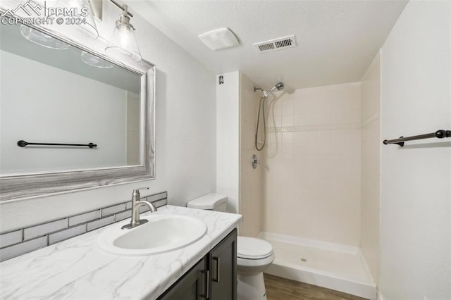 bathroom with hardwood / wood-style floors, vanity, toilet, a textured ceiling, and a tile shower