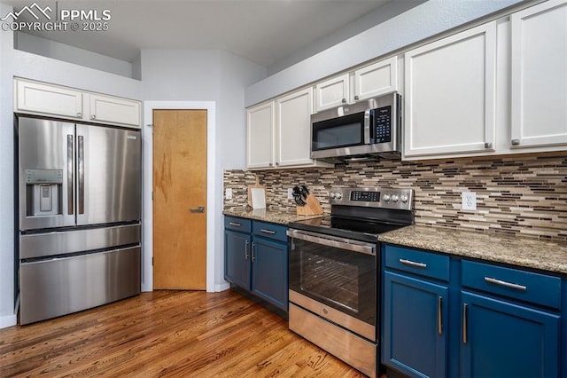 kitchen with blue cabinetry, white cabinetry, light stone countertops, stainless steel appliances, and backsplash