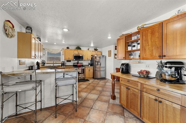 kitchen with a kitchen bar, sink, a textured ceiling, and appliances with stainless steel finishes