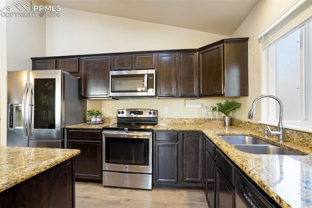 kitchen with light stone counters, stainless steel appliances, vaulted ceiling, sink, and light hardwood / wood-style floors