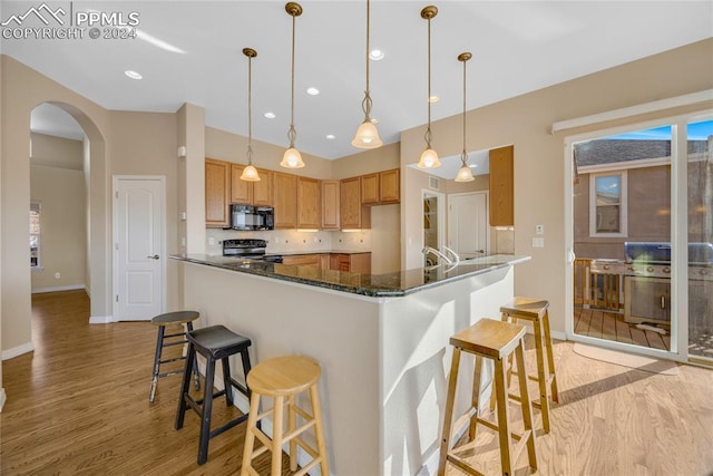 kitchen with backsplash, black appliances, light hardwood / wood-style flooring, dark stone countertops, and hanging light fixtures