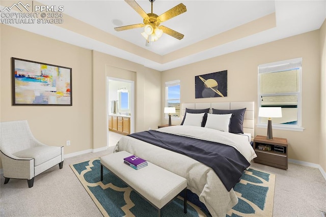 bedroom with connected bathroom, light colored carpet, a raised ceiling, and ceiling fan