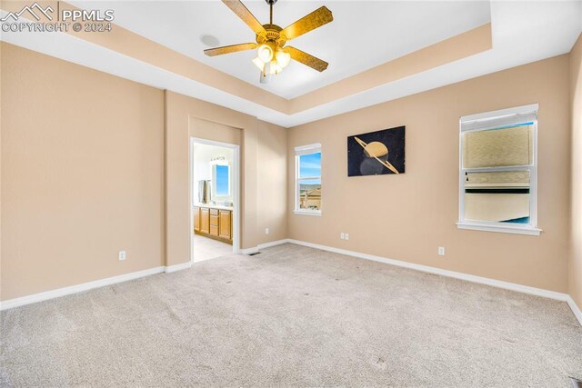 carpeted empty room with a raised ceiling and ceiling fan