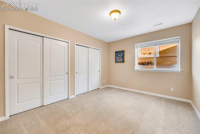 unfurnished bedroom with light carpet and multiple closets