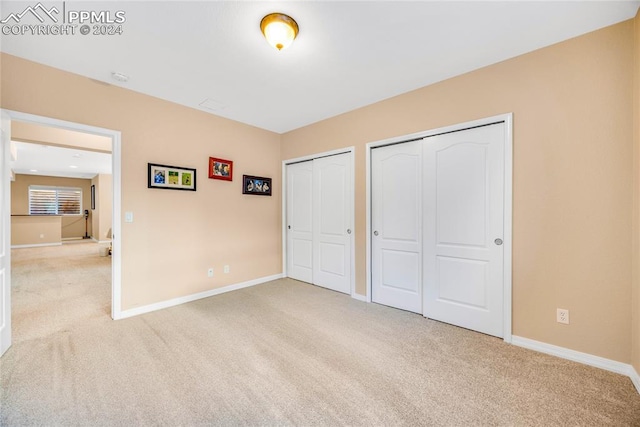 unfurnished bedroom featuring light carpet and multiple closets