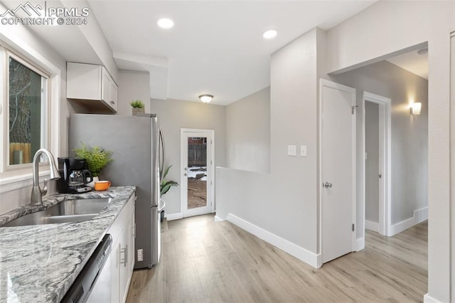 kitchen with white cabinets, light wood-type flooring, light stone countertops, and sink