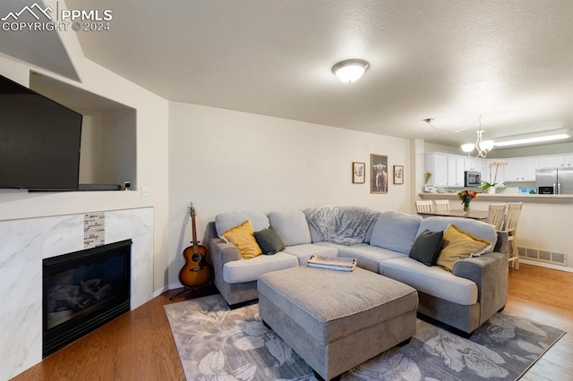 living room featuring a textured ceiling, light hardwood / wood-style floors, a notable chandelier, and a premium fireplace