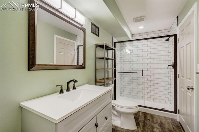 bathroom featuring wood-type flooring, vanity, toilet, and a shower with shower door