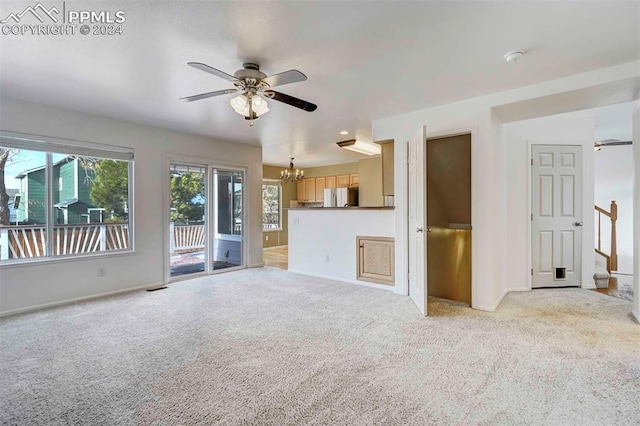 unfurnished living room with ceiling fan with notable chandelier and light colored carpet