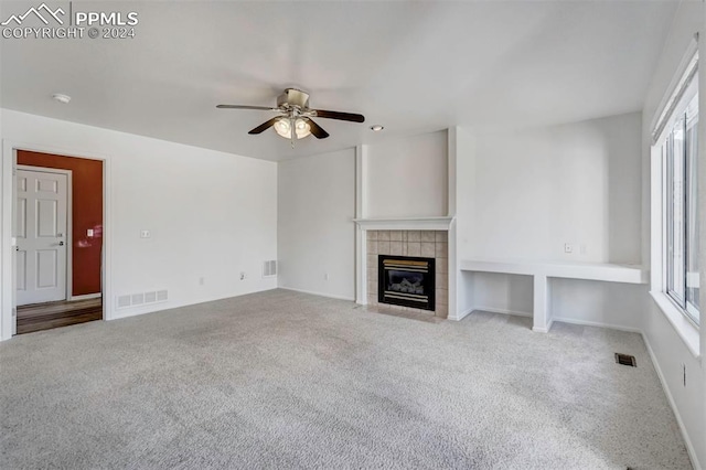 unfurnished living room with a tiled fireplace, ceiling fan, plenty of natural light, and light carpet