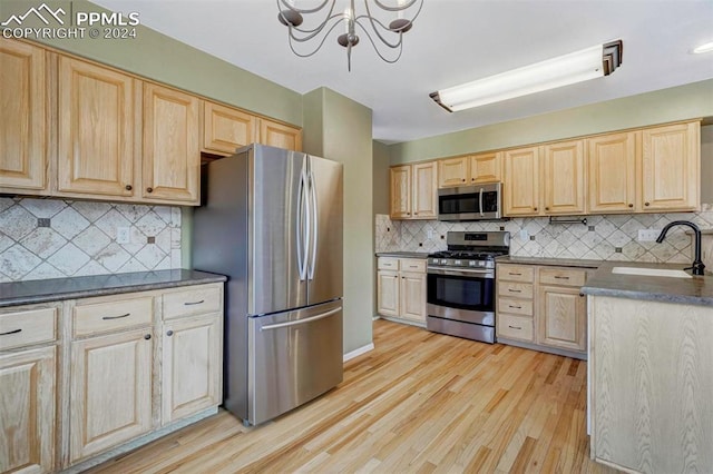 kitchen featuring an inviting chandelier, sink, light hardwood / wood-style flooring, tasteful backsplash, and stainless steel appliances