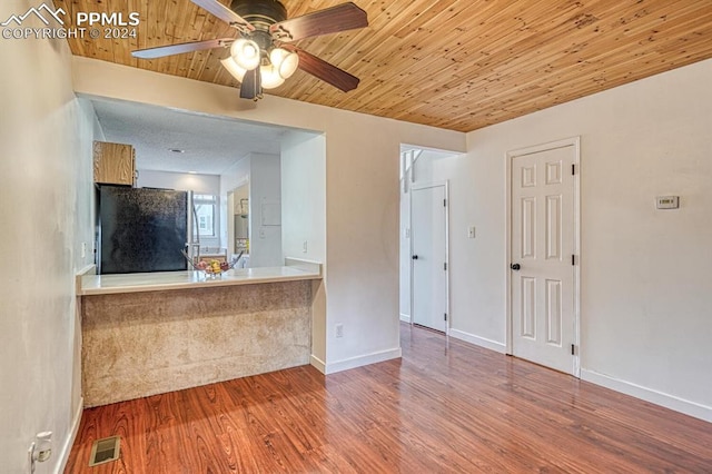 kitchen featuring ceiling fan, kitchen peninsula, hardwood / wood-style floors, black refrigerator, and wood ceiling