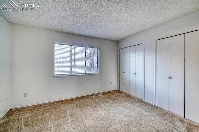 unfurnished bedroom featuring a textured ceiling, light colored carpet, and multiple closets