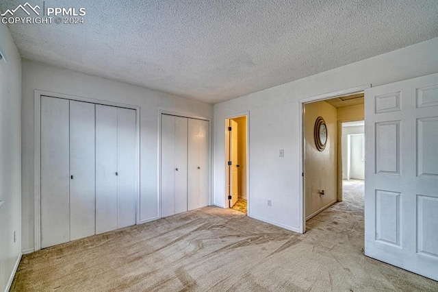 unfurnished bedroom featuring two closets, a textured ceiling, and light colored carpet