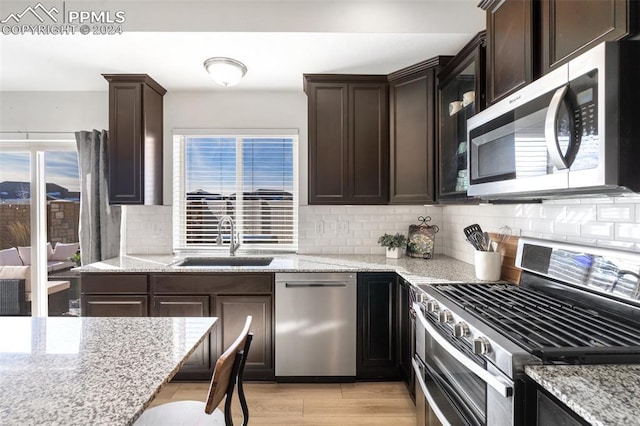 kitchen with dark brown cabinets, sink, light stone counters, and stainless steel appliances