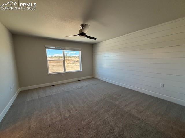 spare room with baseboards, dark carpet, and a ceiling fan