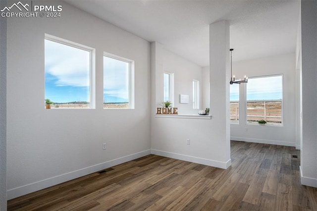 unfurnished room with an inviting chandelier and dark wood-type flooring