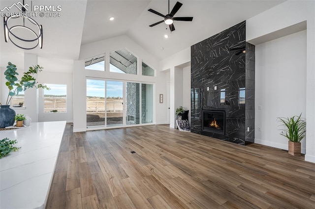 unfurnished living room with high vaulted ceiling, ceiling fan, wood-type flooring, and a high end fireplace