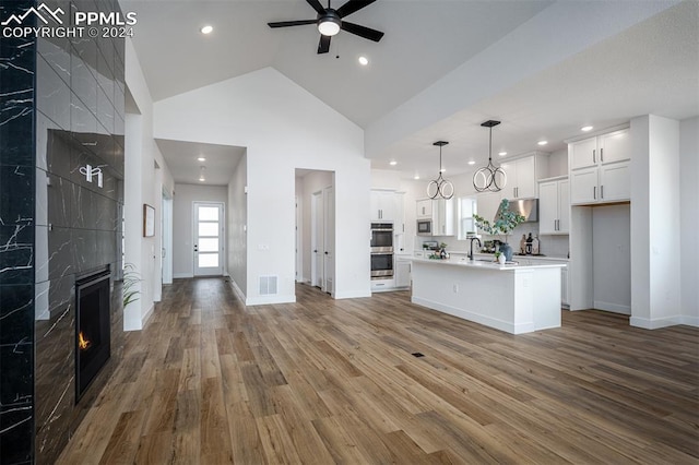 kitchen featuring pendant lighting, a kitchen island with sink, white cabinets, appliances with stainless steel finishes, and wood-type flooring