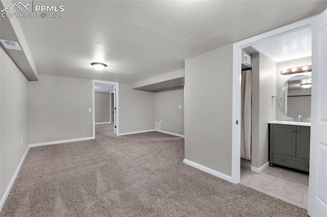 basement with a textured ceiling, sink, and light carpet