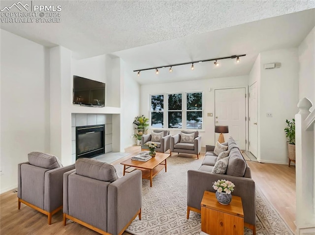 living room featuring a tile fireplace, a textured ceiling, light wood-type flooring, and rail lighting