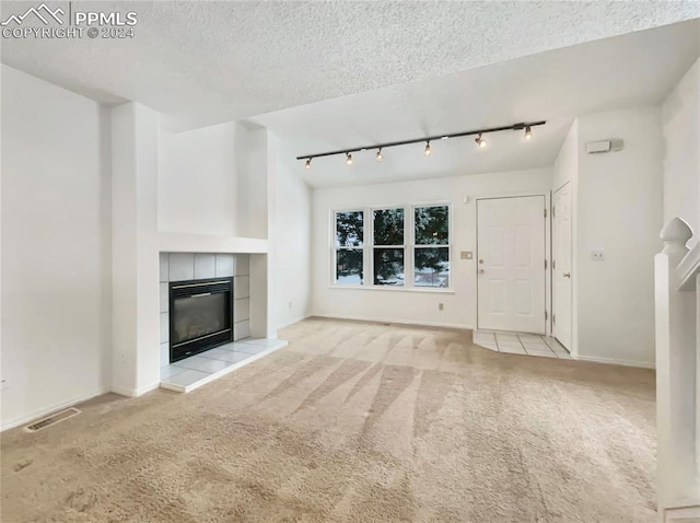 unfurnished living room featuring light carpet, a textured ceiling, track lighting, and a fireplace