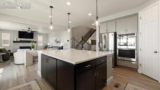 kitchen featuring ceiling fan, light wood-type flooring, appliances with stainless steel finishes, decorative light fixtures, and a kitchen island