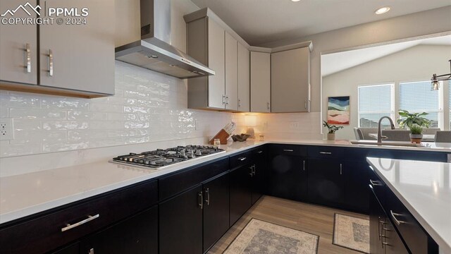 kitchen featuring decorative backsplash, wall chimney exhaust hood, sink, white cabinets, and lofted ceiling