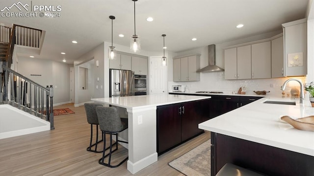 kitchen featuring stainless steel appliances, sink, wall chimney range hood, a center island, and hanging light fixtures