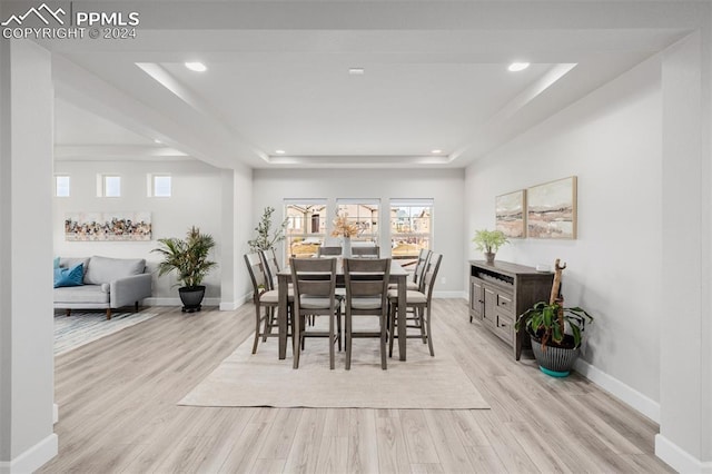 dining space with a raised ceiling and light hardwood / wood-style flooring