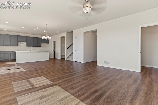 unfurnished living room featuring ceiling fan with notable chandelier and dark wood-type flooring