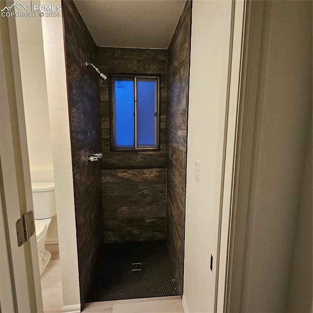 bathroom featuring tiled shower, tile patterned flooring, and toilet