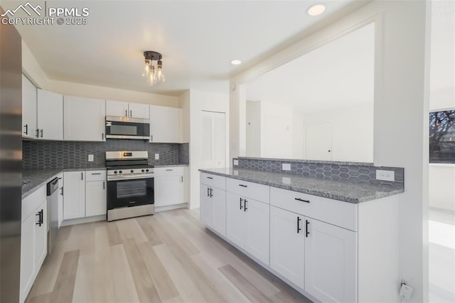 kitchen with dark stone counters, white cabinets, stainless steel appliances, light hardwood / wood-style floors, and backsplash