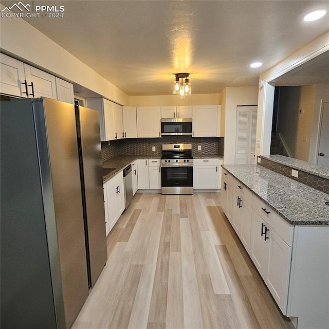 kitchen with white cabinetry, light hardwood / wood-style flooring, dark stone counters, stainless steel appliances, and backsplash