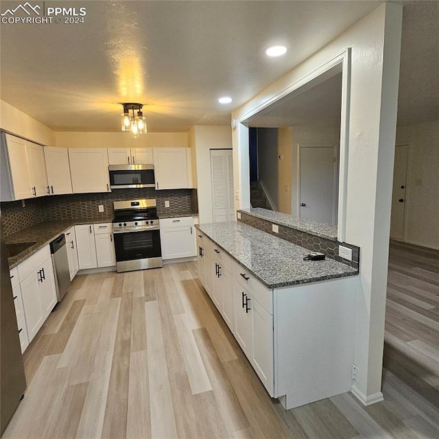 kitchen with white cabinets, appliances with stainless steel finishes, light wood-type flooring, and backsplash