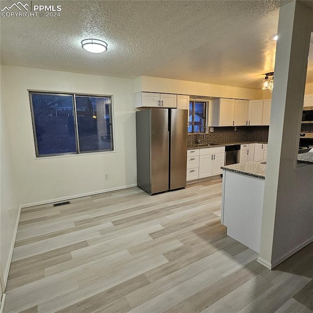 kitchen featuring dark stone countertops, a textured ceiling, decorative backsplash, white cabinets, and appliances with stainless steel finishes