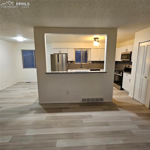 kitchen with white cabinets, backsplash, appliances with stainless steel finishes, and a textured ceiling