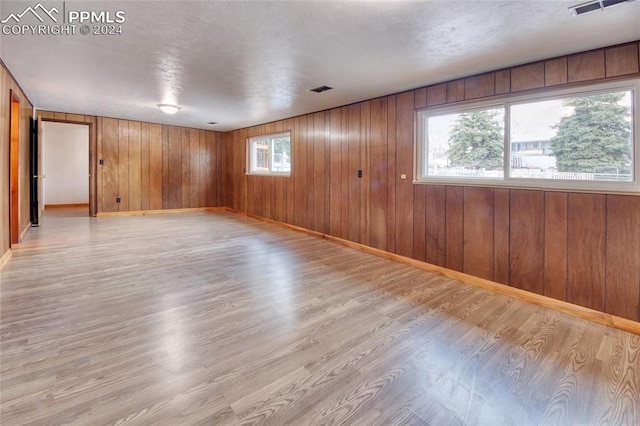 unfurnished room with wood walls, plenty of natural light, and light hardwood / wood-style floors