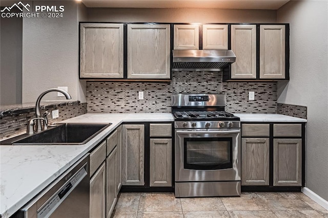 kitchen with exhaust hood, sink, decorative backsplash, light stone counters, and stainless steel appliances