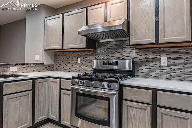 kitchen with light stone countertops, sink, tasteful backsplash, and stainless steel range with gas stovetop