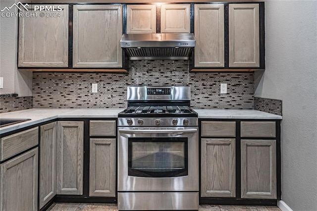 kitchen with light stone counters, backsplash, extractor fan, and stainless steel gas range