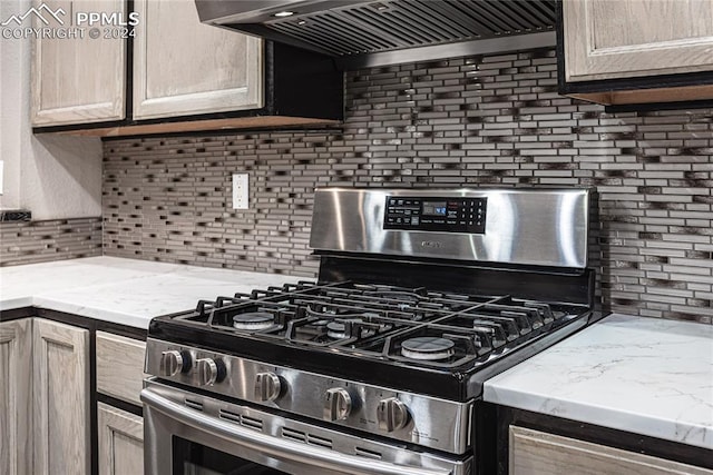 kitchen with tasteful backsplash, wall chimney range hood, light brown cabinetry, and gas range