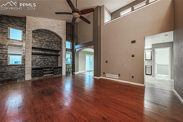 unfurnished living room with ceiling fan, high vaulted ceiling, a textured ceiling, and hardwood / wood-style flooring