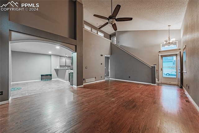 unfurnished living room featuring ceiling fan with notable chandelier, wood-type flooring, a textured ceiling, and high vaulted ceiling