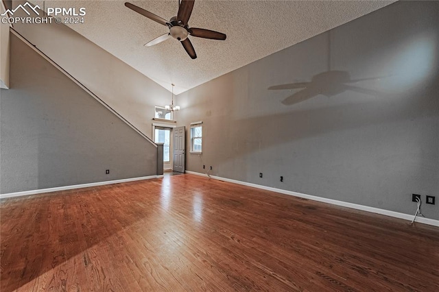 spare room featuring ceiling fan with notable chandelier, high vaulted ceiling, wood-type flooring, and a textured ceiling