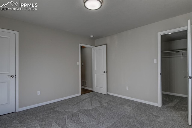 unfurnished bedroom featuring a walk in closet, dark carpet, and a closet