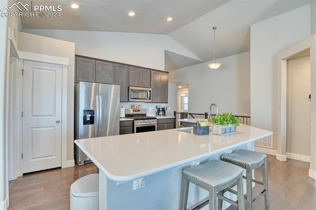 kitchen with decorative light fixtures, a center island with sink, stainless steel appliances, and vaulted ceiling